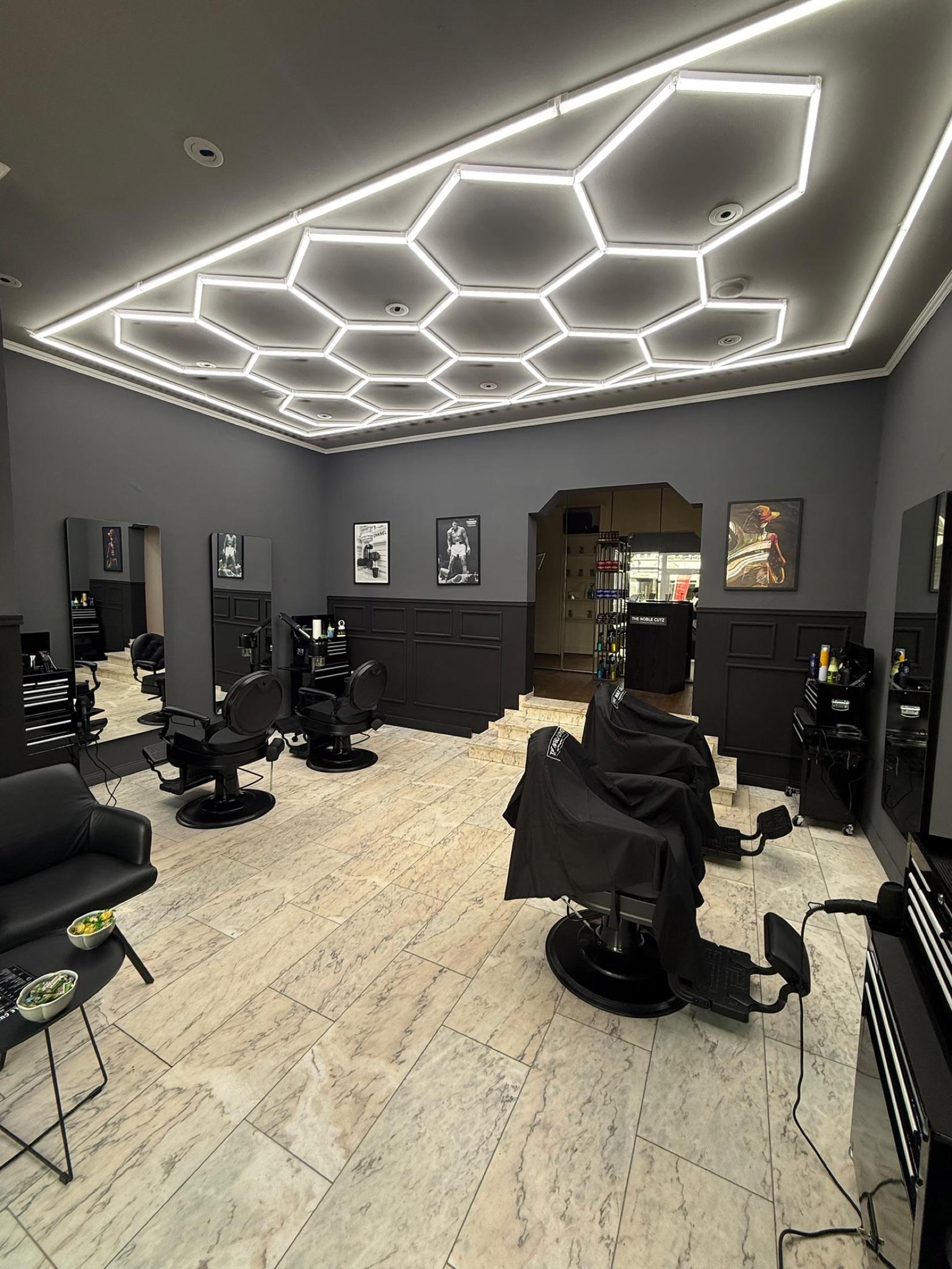 Innenraum des THE NOBLE CUTZ Barbershops in Hamburg-Winterhude mit Hexagon-LED-Decke und Barber-Chairs